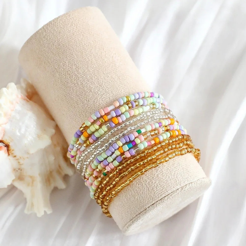 A stack of colorful beaded bangles resting on a beige cylindrical object next to a piece of white shell.