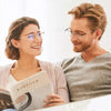 A smiling woman and man looking at a book together, with the woman holding photochromic progressive reading glasses.