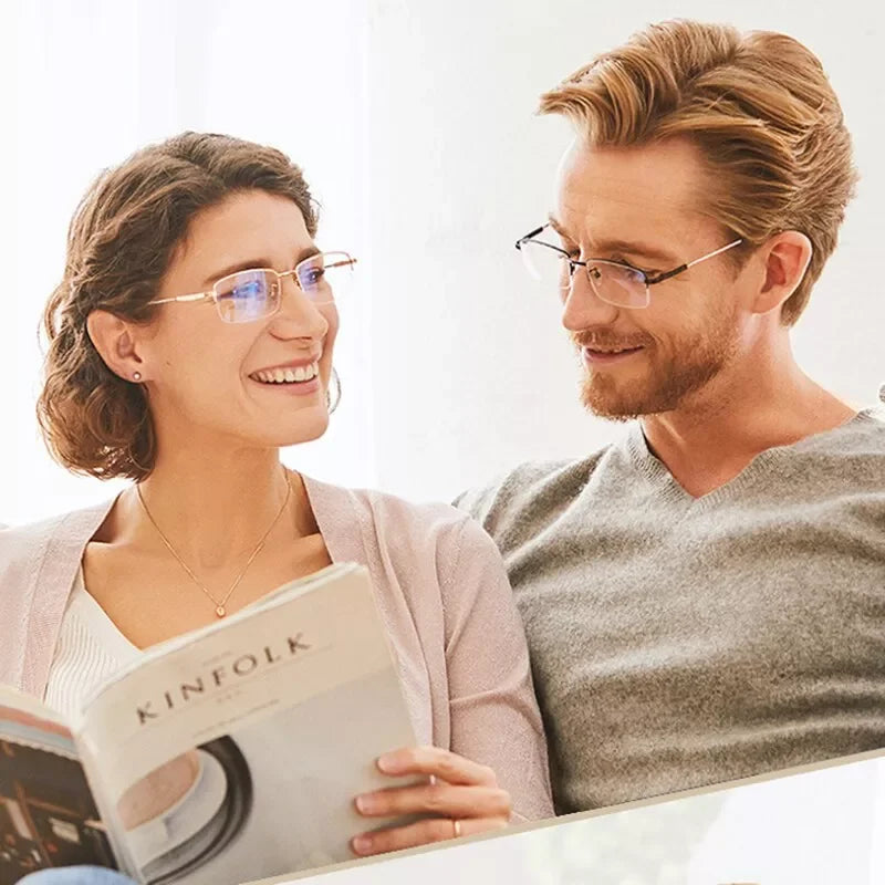 A smiling woman and man looking at a book together, with the woman holding photochromic progressive reading glasses.