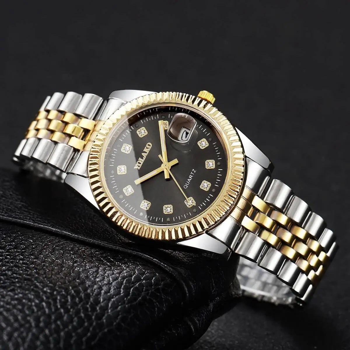 A gold-toned quartz wristwatch with a black dial and rhinestone accents is shown on a black leather strap.