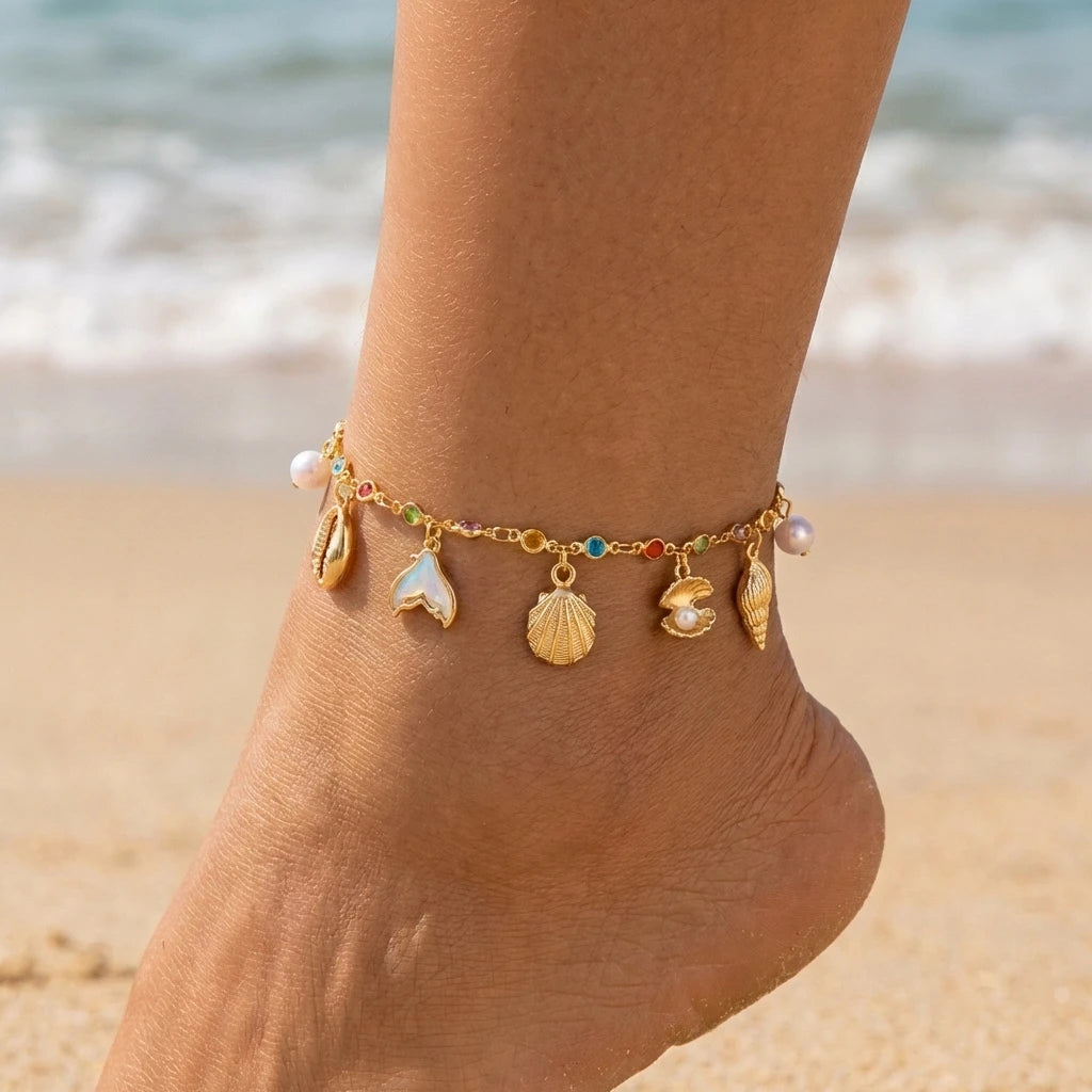 Gold and pearl bohemian starfish conch anklet worn on a person's ankle near the ocean.