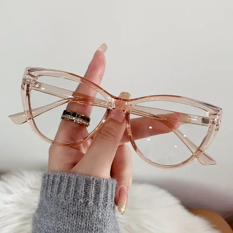Eine Hand hält eine Vintage-Rose-Gold-Cat-Eye-Lesebrille mit klaren Linsen vor weißem Hintergrund.