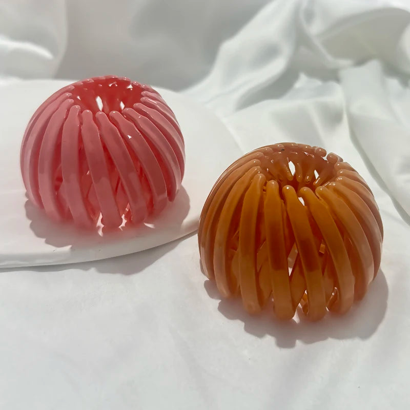 Two spherical hair clips, one pink and one orange, are displayed on a white plate.