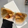 A pair of amber-tinted retro cat eye sunglasses being held by a hand against a white surface.