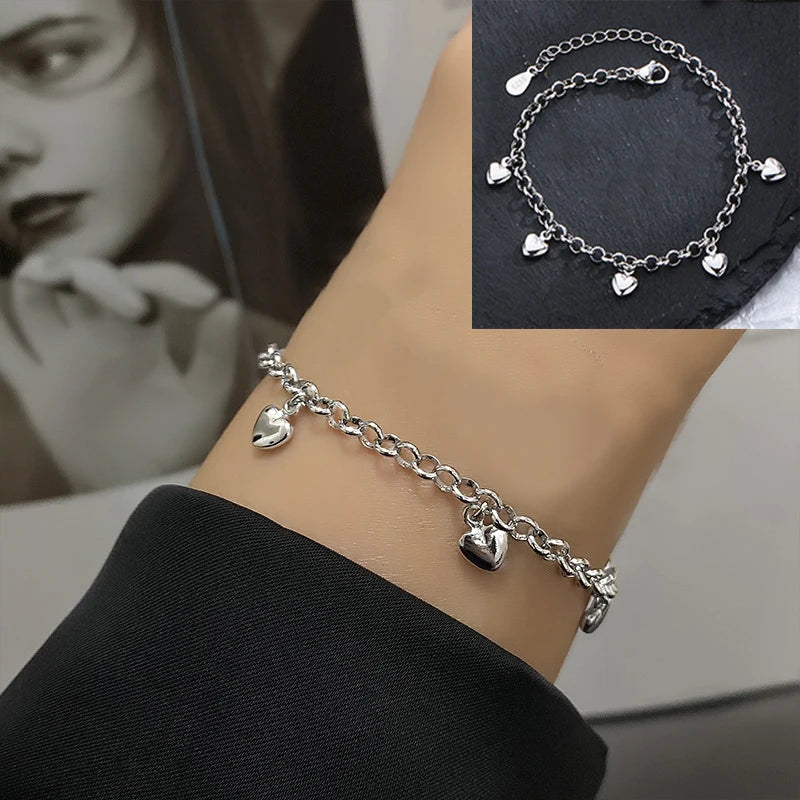 A close-up of a sterling silver double heart charm bracelet worn on a wrist against a dark background.