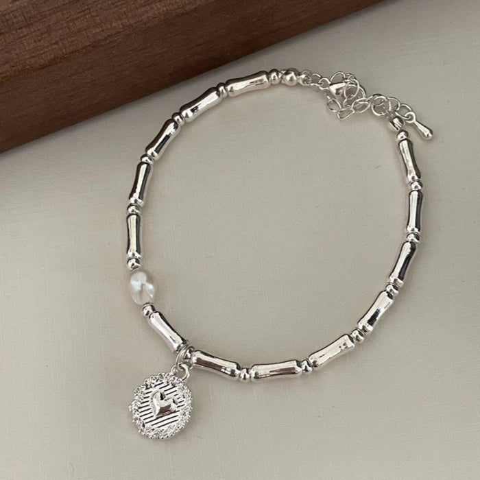 A silver bell bangle bracelet with a pearl drop and an engraved charm displayed on a neutral surface.