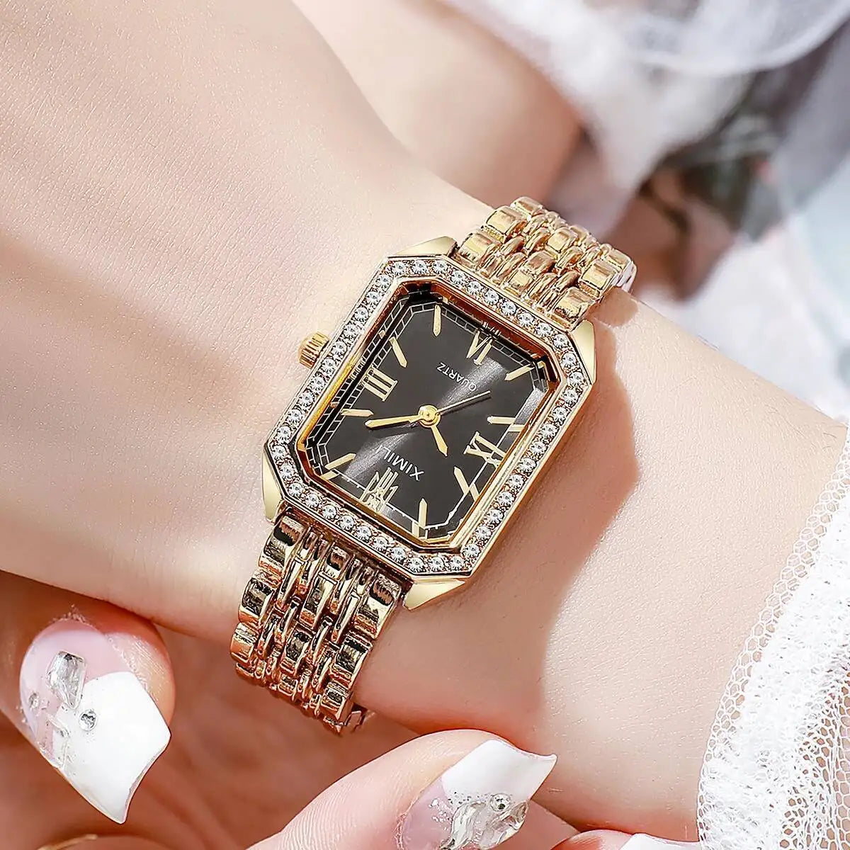 A close-up of a gold-toned rhinestone quartz wristwatch with a black face and gold links on a woman's wrist.