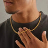Gros plan d'un homme portant un collier en corde torsadée en acier inoxydable plaqué or 18K sur un t-shirt sombre.