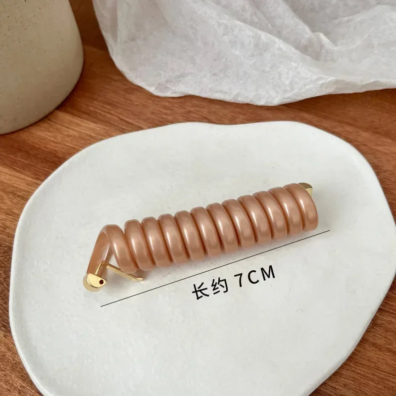A long, light pink rubber braided ponytail holder measuring 7cm resting on a white ceramic plate.