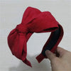 A red fabric wide bow headband worn on a hand.