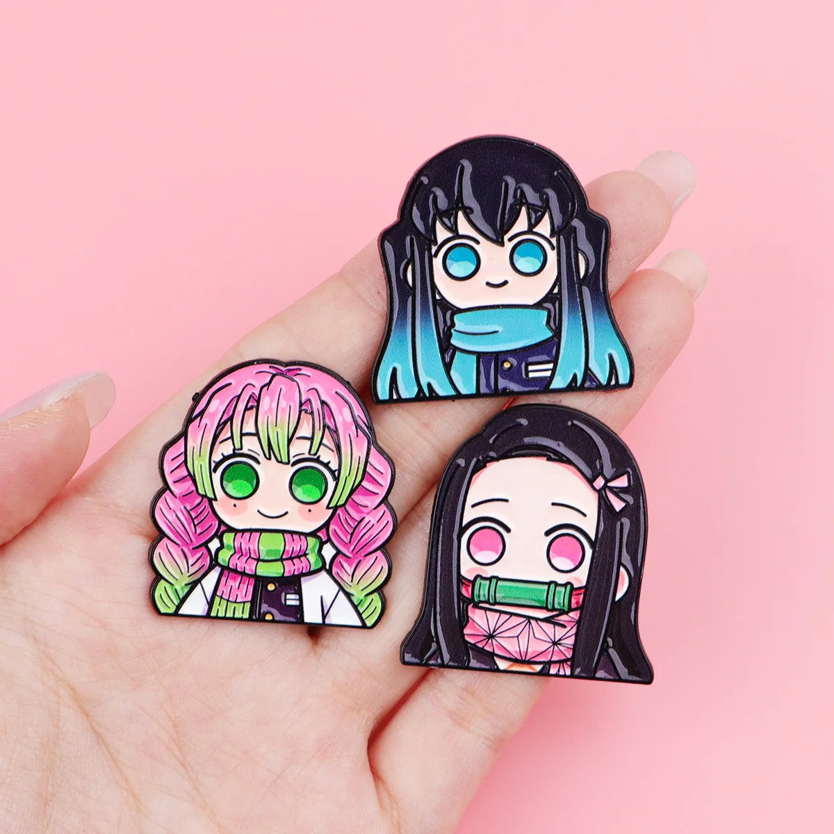 A hand holds a set of 12 anime enamel pin brooches featuring characters with dark hair and bright pink and teal accents.