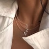 A close-up of a delicate mother of pearl initial necklace with crystal accents worn around the neck.