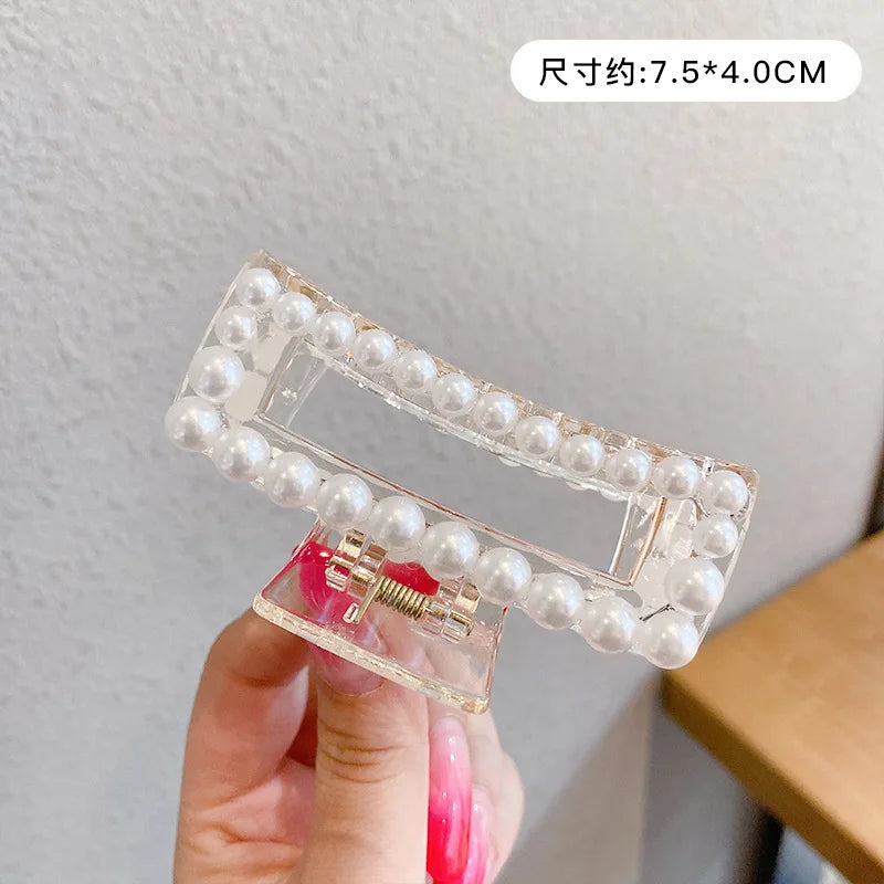 A hand holds a clear plastic hair claw accessory decorated with small white simulated pearls.