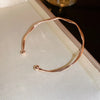 A minimalist gold-tone twisted cuff bangle displayed in a light box.