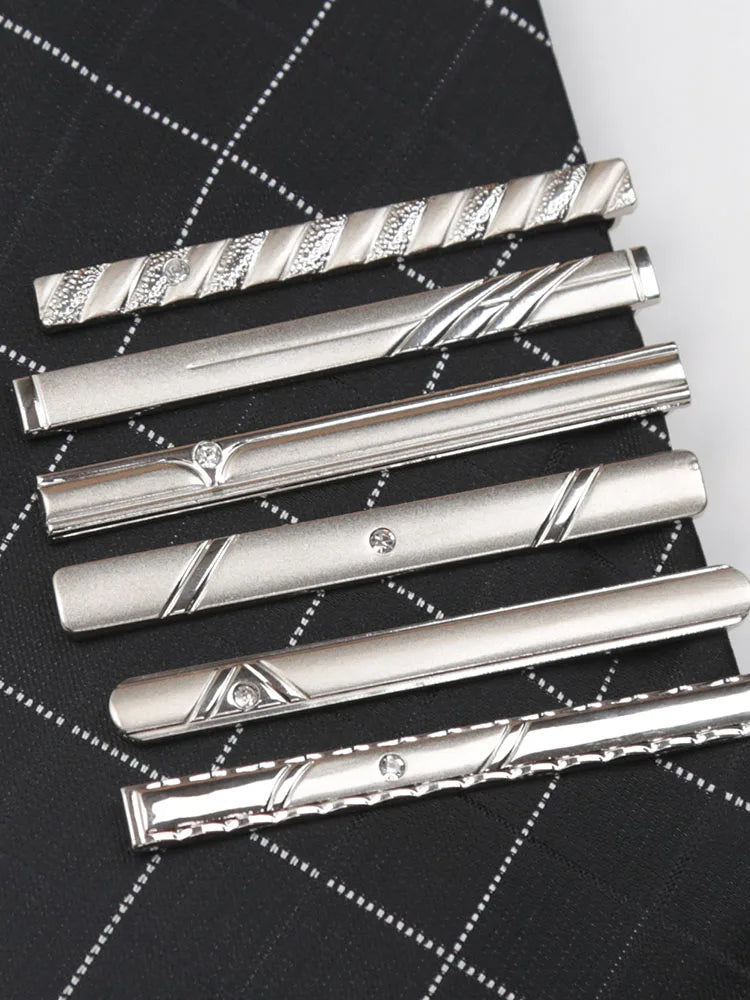 A collection of silver metal tie clips displayed diagonally on a black plaid fabric background.