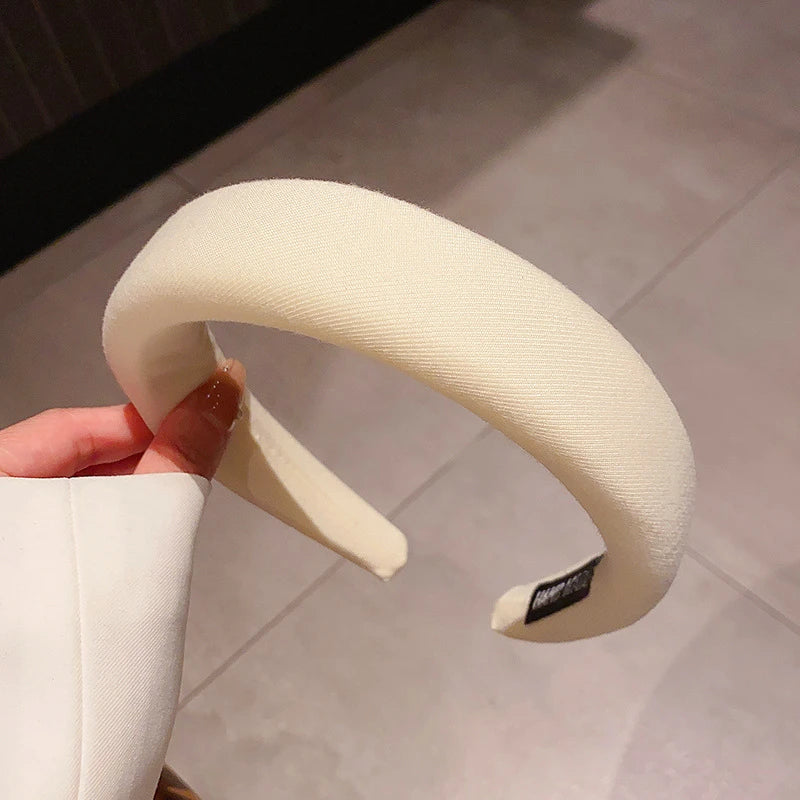 Gros plan d'un bandeau pour cheveux épaissi de couleur crème tenu par une main.