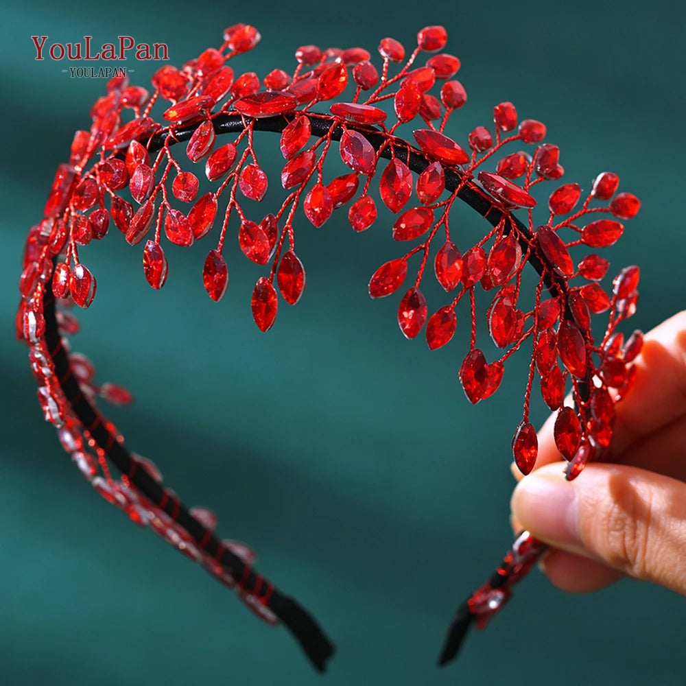 A close-up of a red rhinestone bridal headband featuring delicate floral designs, held by a hand.