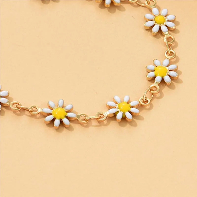 A delicate gold chain anklet featuring small yellow and white enamel daisy charms.