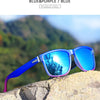 Blue and purple polarized sunglasses resting on a light-colored rock against a blurred green landscape.
