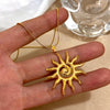 Une main tient un collier fleur de soleil en spirale plaqué or avec une fine chaîne dorée.