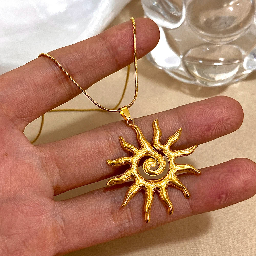 Une main tient un collier fleur de soleil en spirale plaqué or avec une fine chaîne dorée.