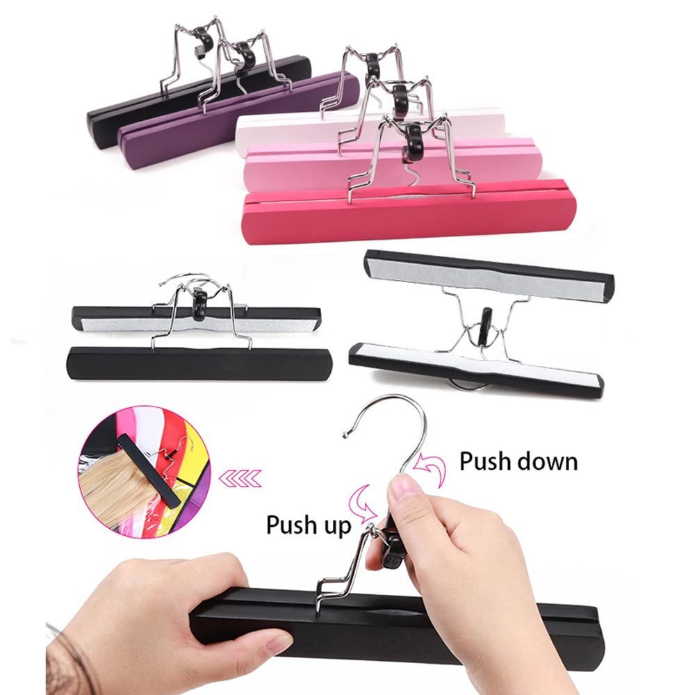 Various colored metal hair extension holders and a black holder being used to push down a wooden wig.