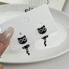 A pair of black cat stud earrings is displayed on a white card on a white plate.
