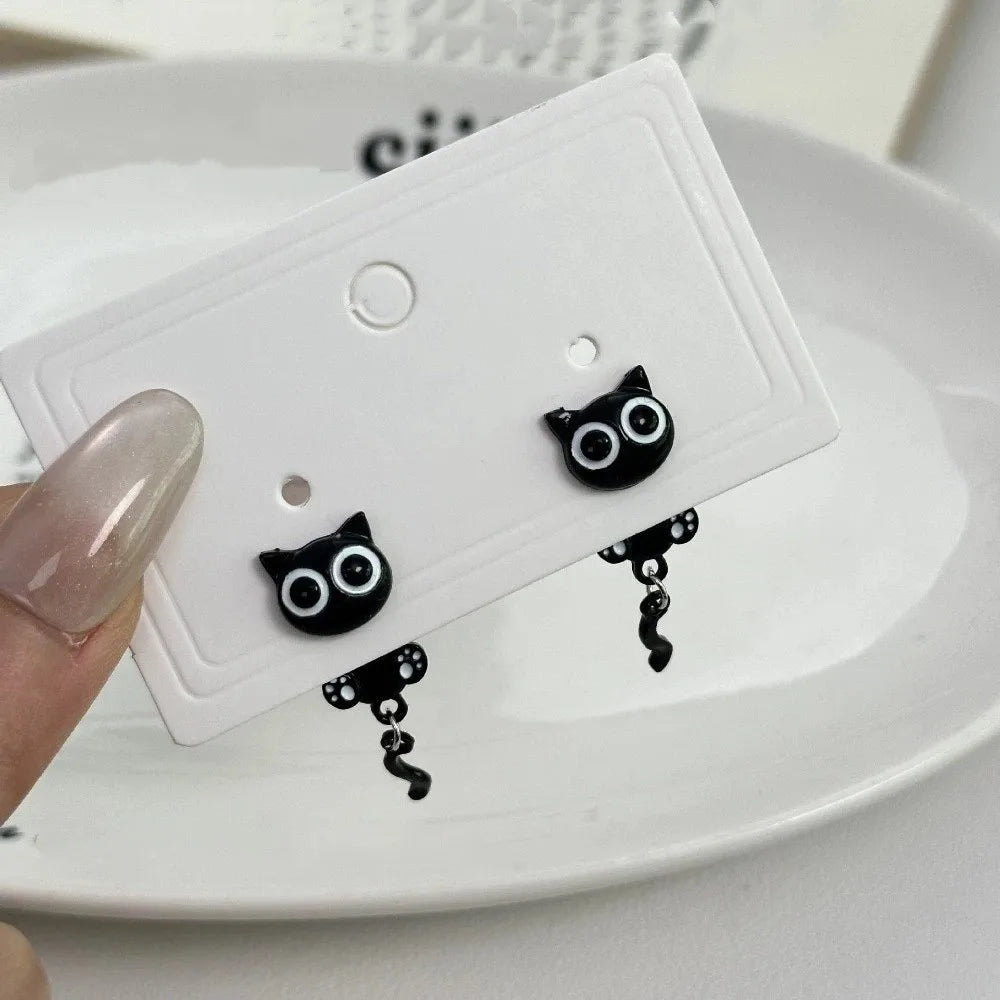 A pair of black cat stud earrings is displayed on a white card on a white plate.