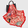 A luxury silk square scarf in red and pink floral patterns draped over a black bag.