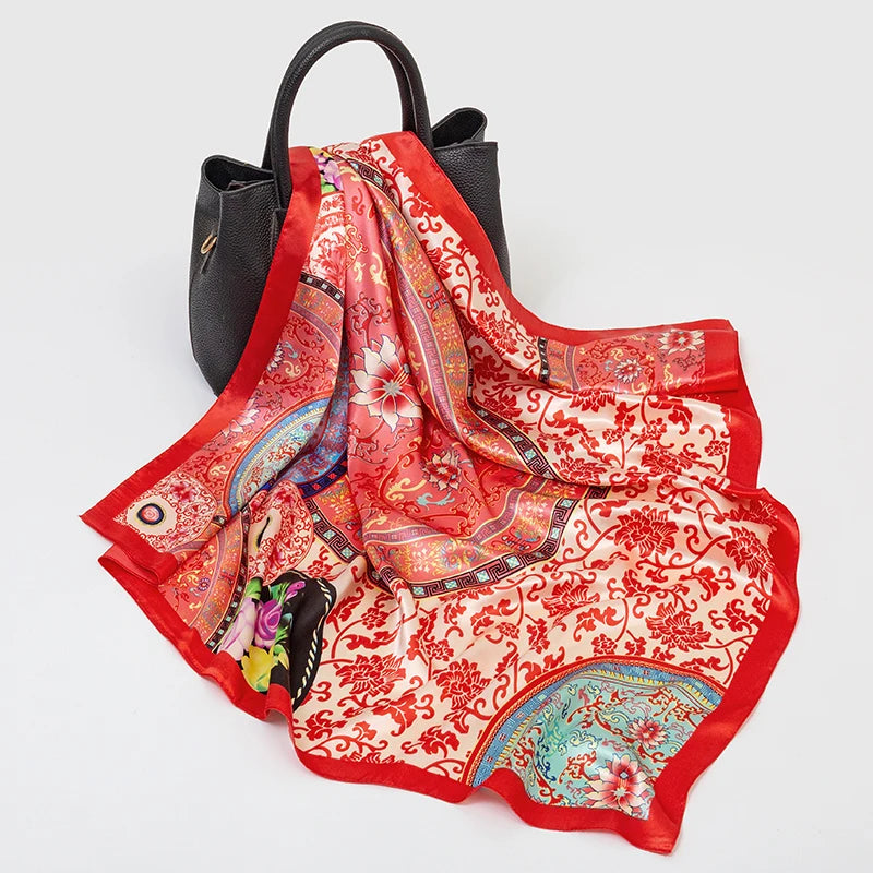 A luxury silk square scarf in red and pink floral patterns draped over a black bag.