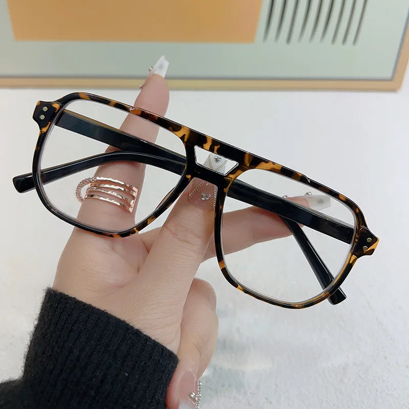 Una mano sostiene unas gafas de lectura estilo piloto vintage con patrón de tortuga.