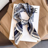 A navy and white floral print silk scarf tied in a knot, displayed on a white background next to a beige blazer.