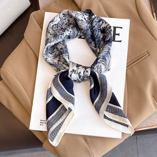 A navy and white floral print silk scarf tied in a knot, displayed on a white background next to a beige blazer.