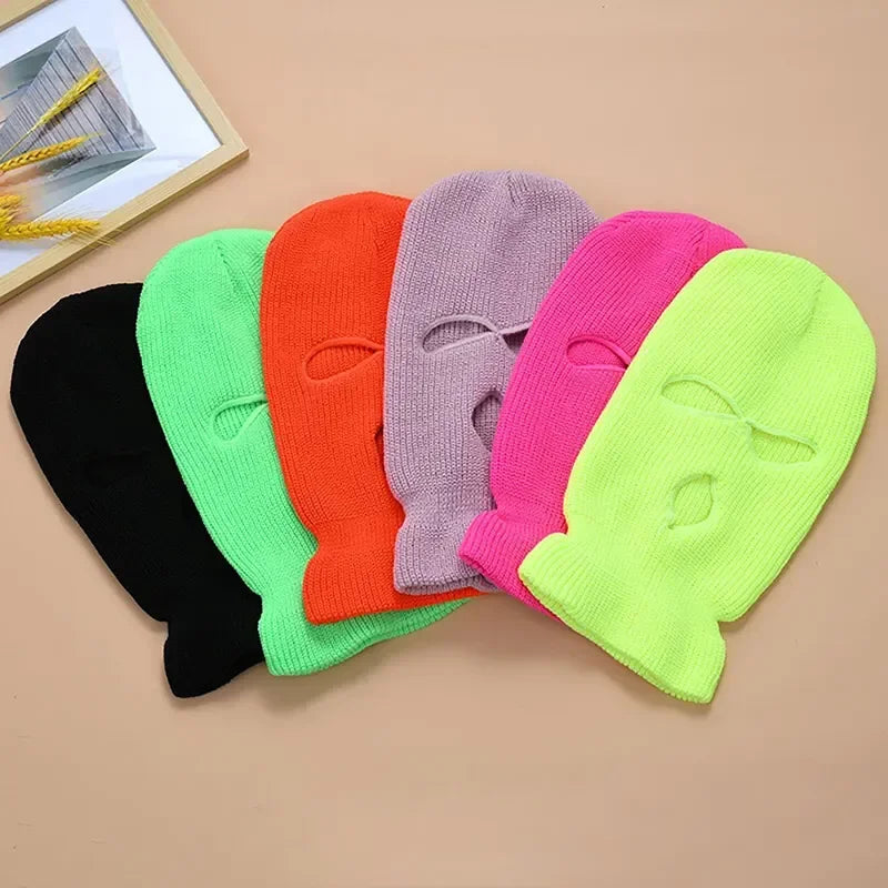 Eine Sammlung farbenfroher Strick-Balaclavas und winddichter Skimasken auf hellem Hintergrund.