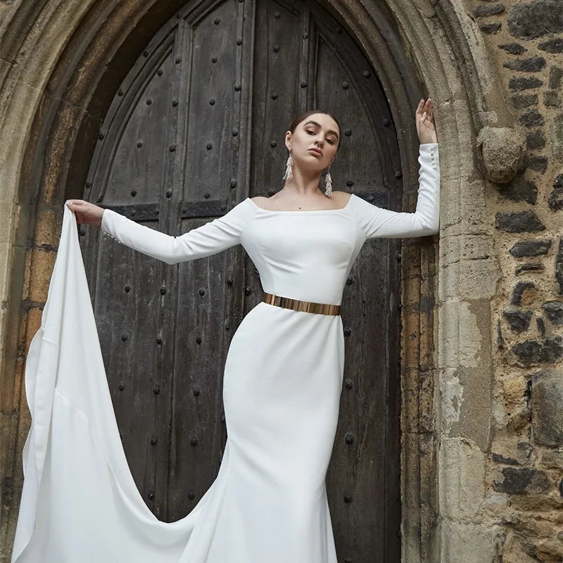 Une mannequin portant une robe blanche avec une ceinture en chaîne dorée, debout dans une arche de pierre.