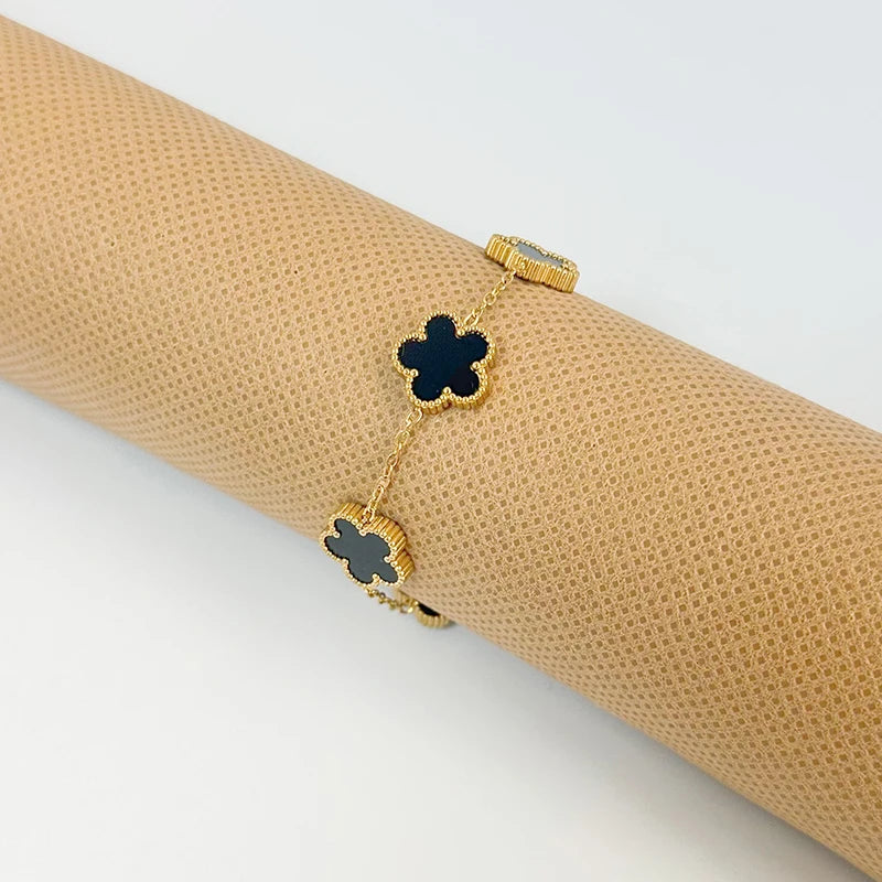 Gold plated stainless steel double-sided petal bracelet with black and gold accents shown on a beige rolled fabric.