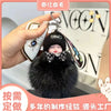 A black fluffy cartoon plush doll keychain is being held next to a white car key fob.