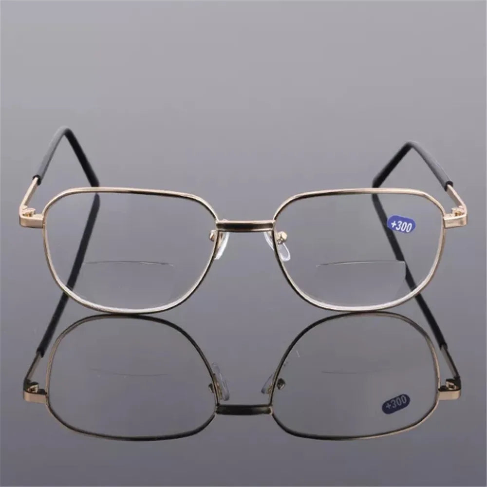 A pair of thin, gold-rimmed bifocal reading glasses resting on a reflective surface.