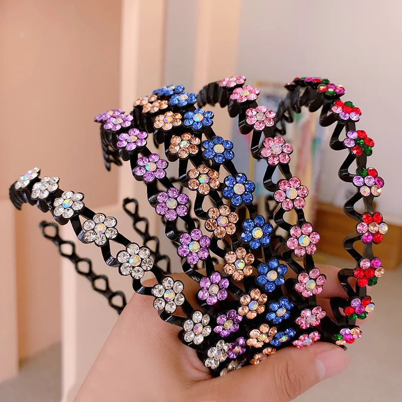 A hand holds a black elastic hair hoop decorated with colorful sparkling rhinestones and small flowers.