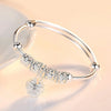 A close-up of a silver bell bangle bracelet with intricate floral engravings resting on a light surface.