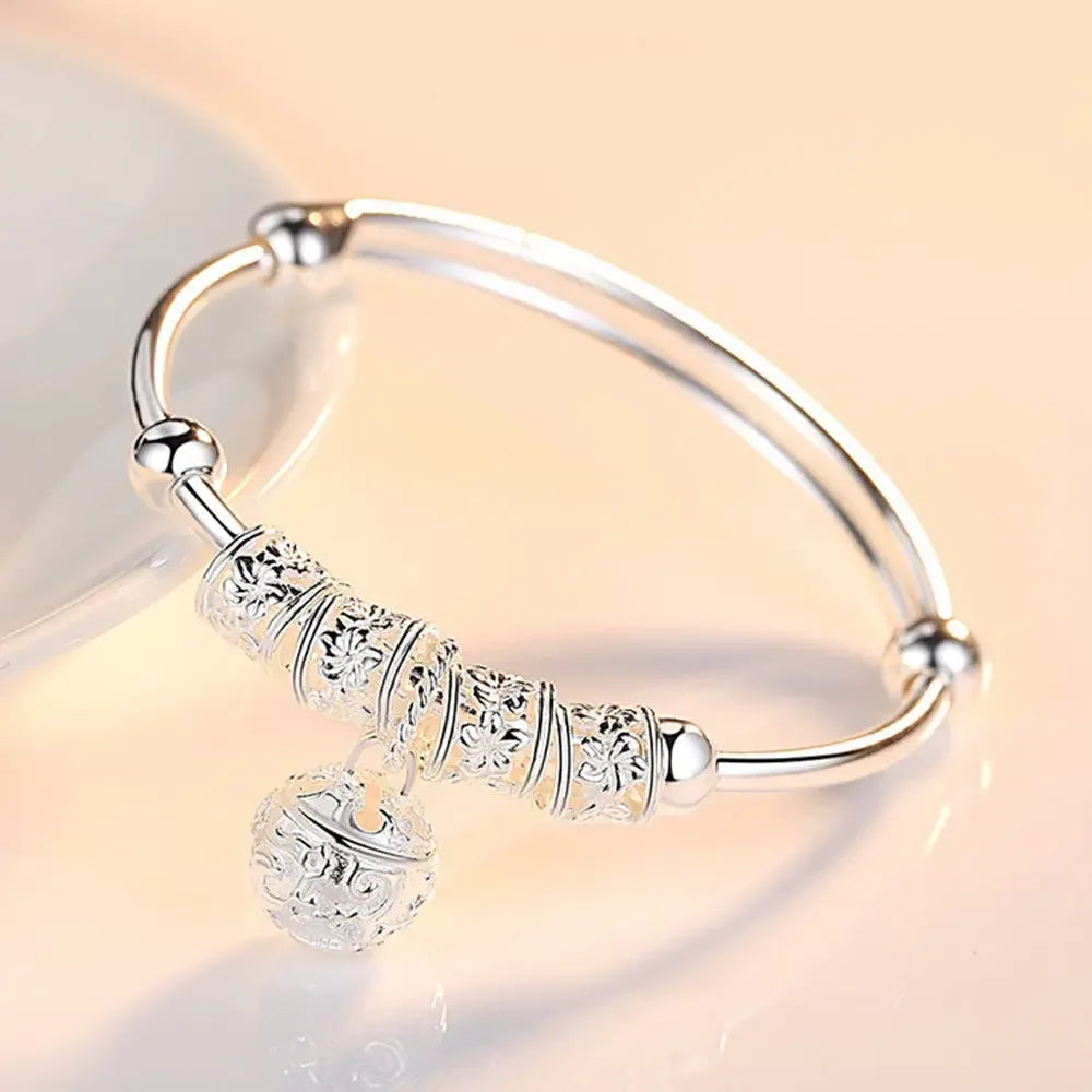 A close-up of a silver bell bangle bracelet with intricate floral engravings resting on a light surface.