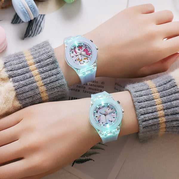 A close-up of a light blue unicorn fashion watch worn on a wrist, next to a knitted sleeve.