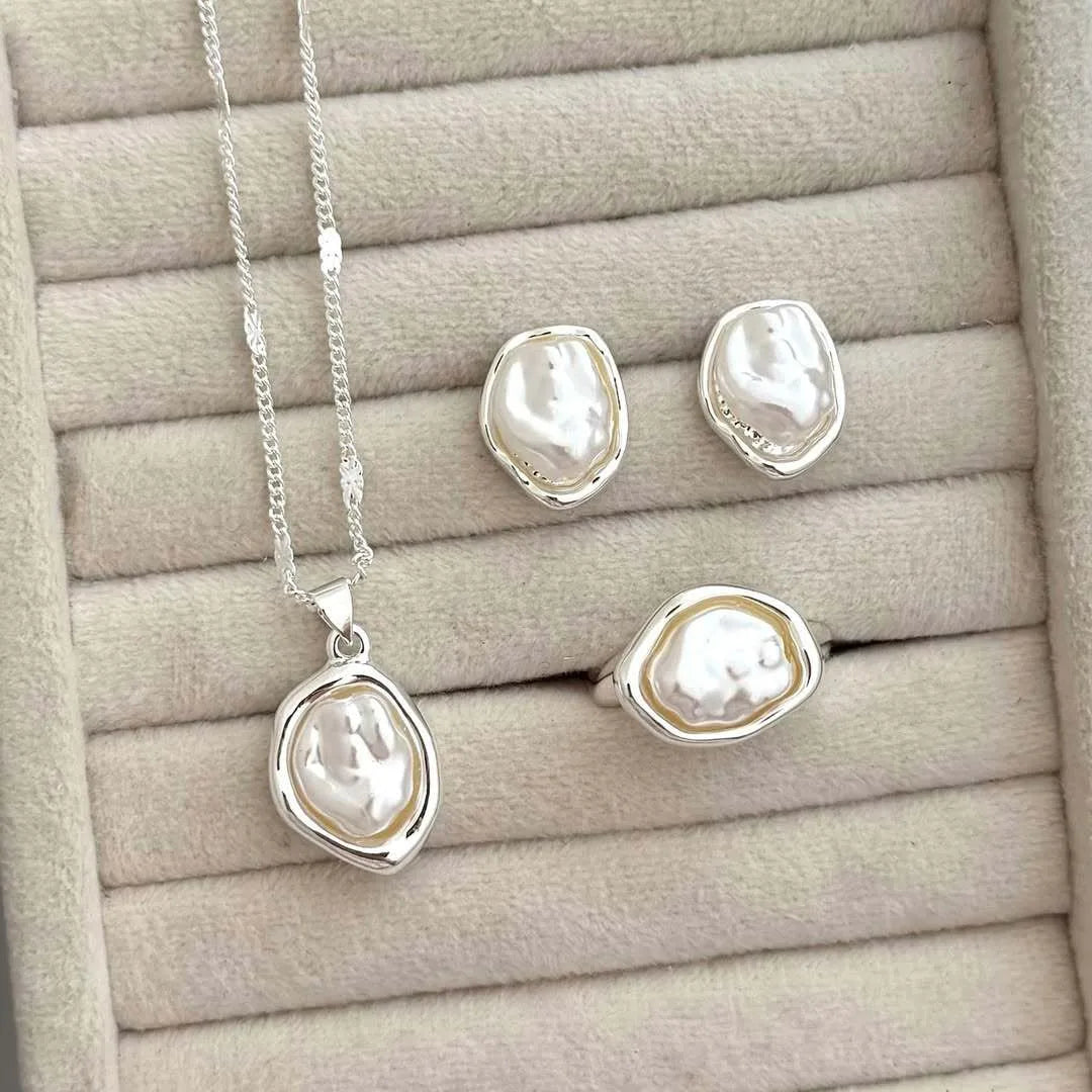 A set of three imitation pearl jewelry pieces including a necklace and two stud earrings displayed on a beige surface.