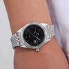 A silver-toned luxury quartz men's wristwatch with a black dial and metal bracelet worn on a wrist.