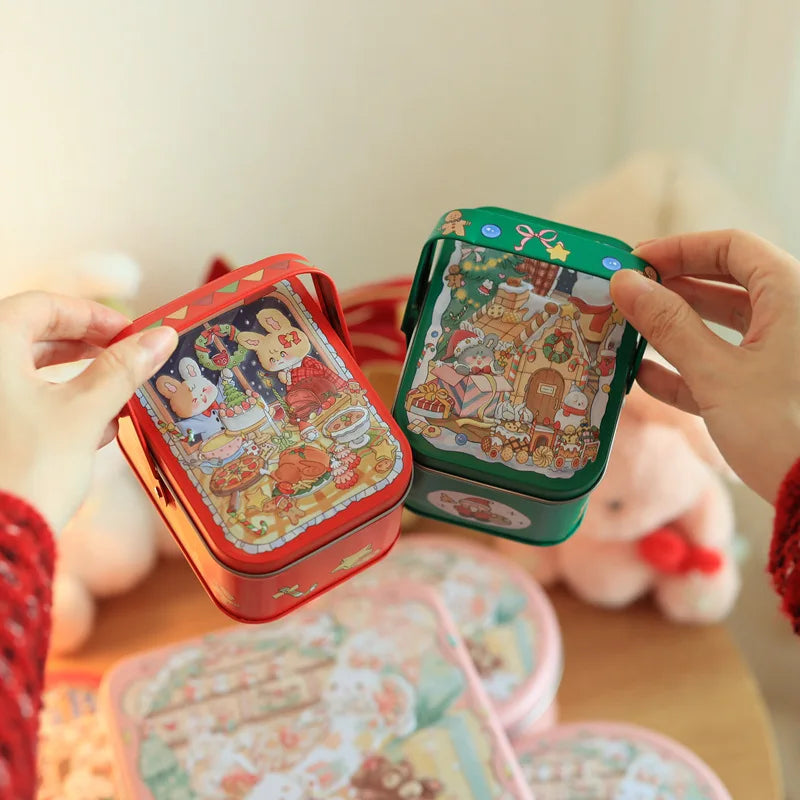 Hands hold a decorative tinplate candy box with a carrying loop, featuring colorful illustrations.