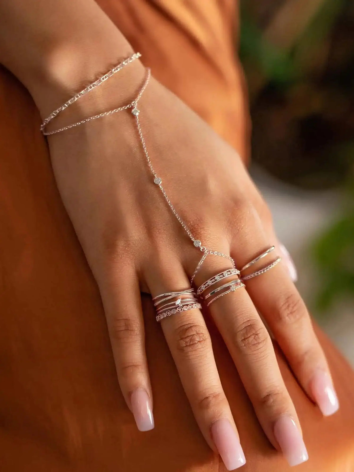 A hand wearing a delicate sterling silver geometric bezel charm bracelet on a person's wrist.