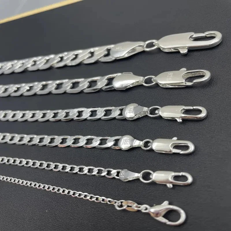 A collection of silver geometric face chain necklaces displayed on a dark background.