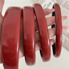 A hand holds four glossy red PU leather fashion headbands for women.