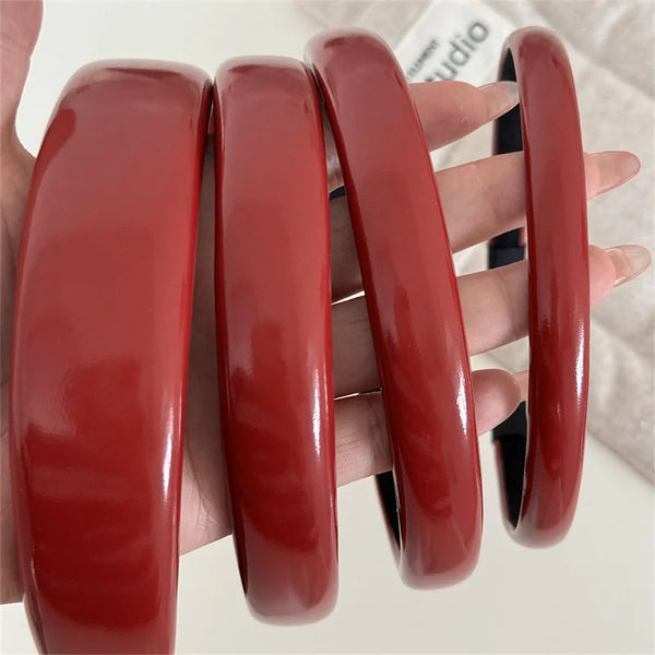 Una mano sostiene cuatro diademas de cuero sintético rojo brillante para mujeres.
