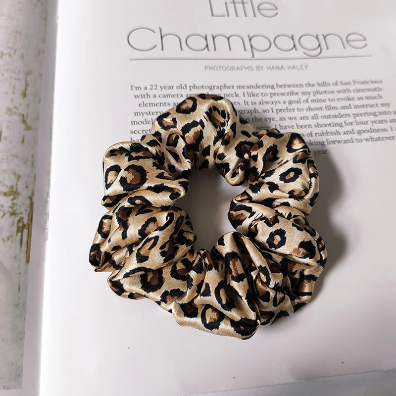 Primer plano de una cinta para el cabello de seda con estampado de leopardo negro y beige, enrollada en un nudo decorativo.